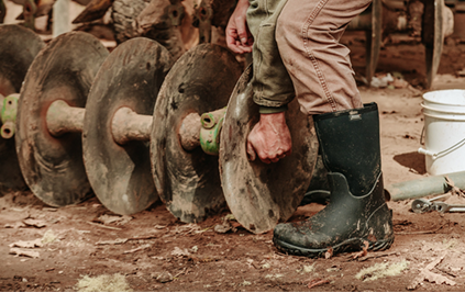 Image features a man lifting a piece of farming equipment while wearing BOGS seamless boots.