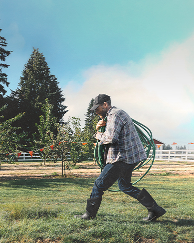 Shop our favorite spring styles featuring a man carrying a garden hose across a yard. 
