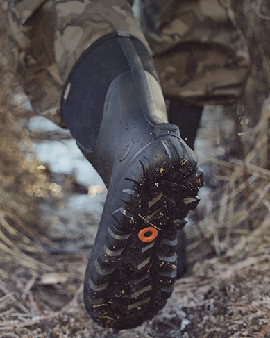 Image features a man wearing a black boot through dried brush.