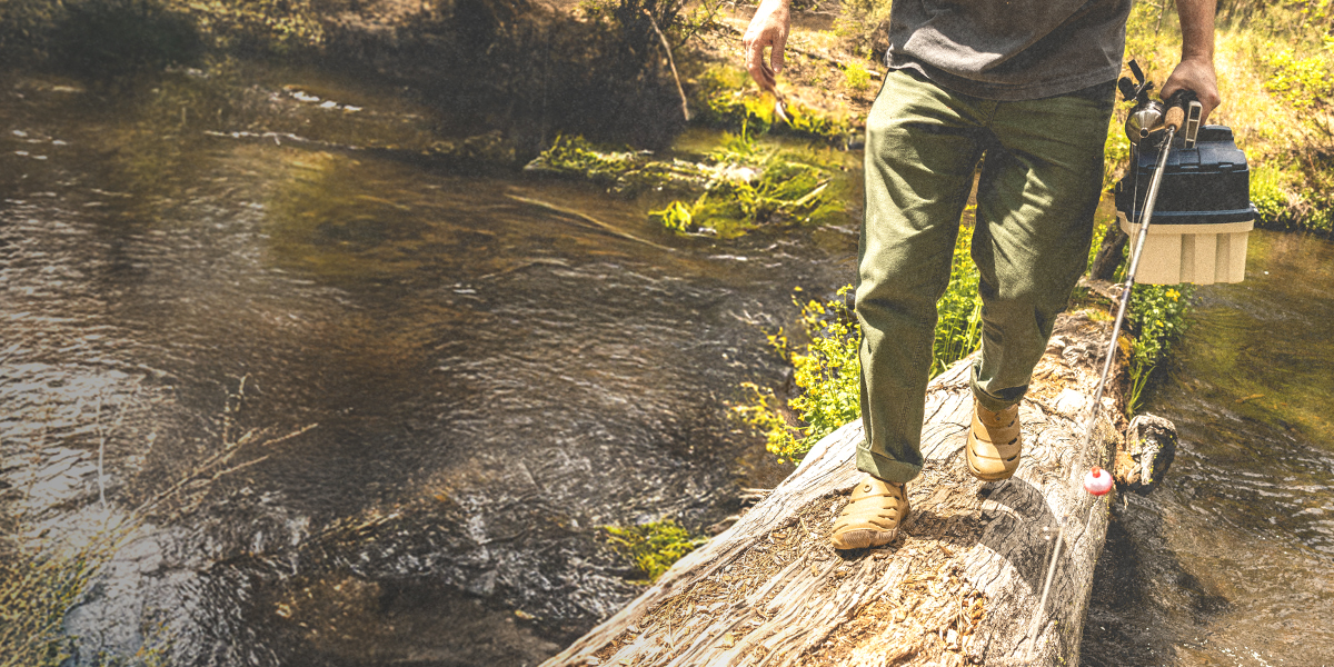 Image features a man walking across a log in a creek wearing the Boga slip on.