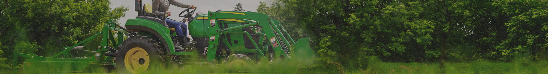 Image features a woman driving a John Deere tractor in a grassy area.