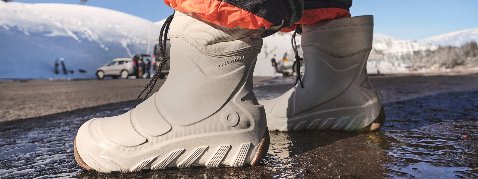 Introducing the boga boot. It's Lighter than it looks. Image shows a person getting into their boga boots in a wet snowy parking lot.