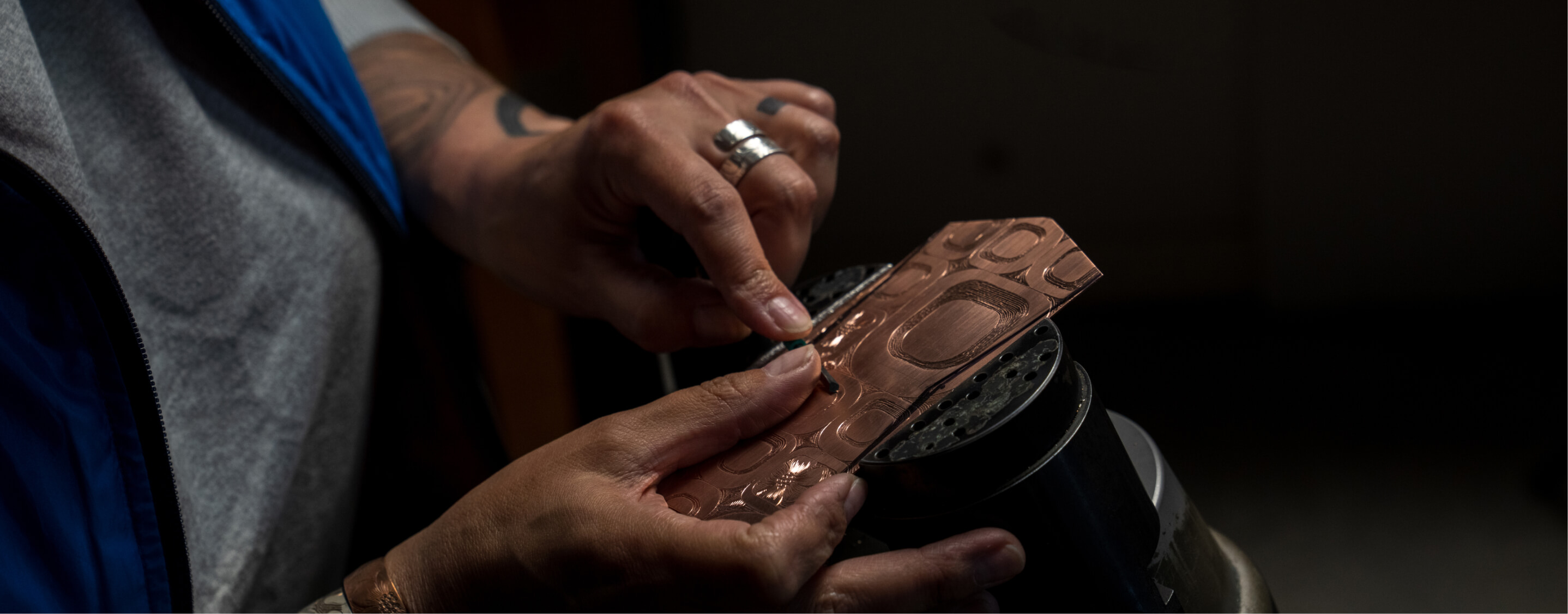 The image shown is a close up of the of Tlingit jeweler Jennifer Younger who is holding the Tlingit formline ovoid design that was originally drawn on copper. 