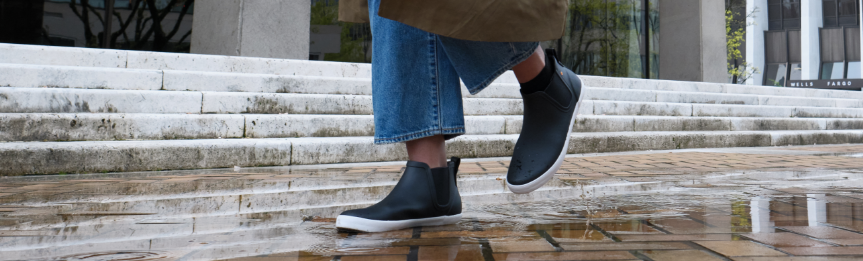 Image features a woman wearing Kicker Rain Chelsea Boots and walking through a puddle.