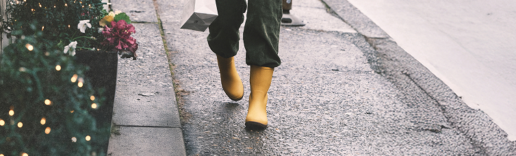 Image features a model walking down a                sidewalk while wearing yellow BOGS rainboots.